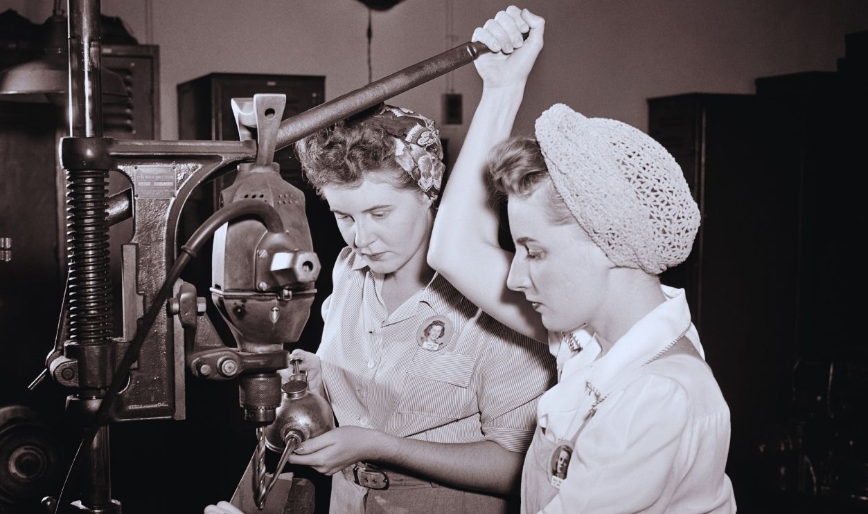 Gettyimages - 1477087913, War Work 1940s two girls in overalls work and clothes hairnet and scarf operating a drill press and oil can female defensive workers.