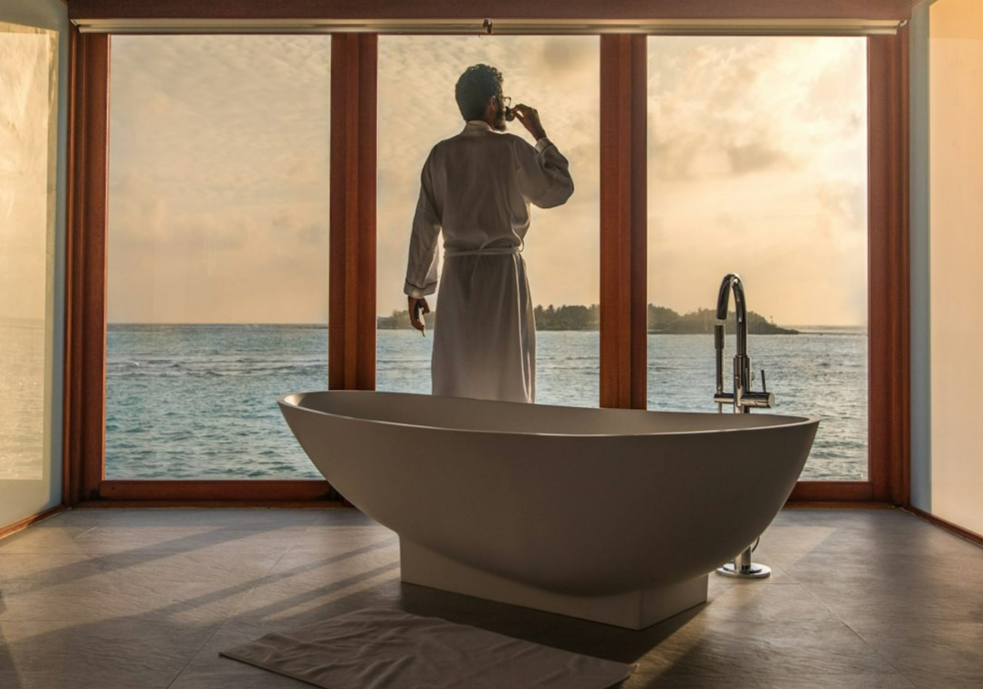man standing in bathroom with bathtub next to body of water