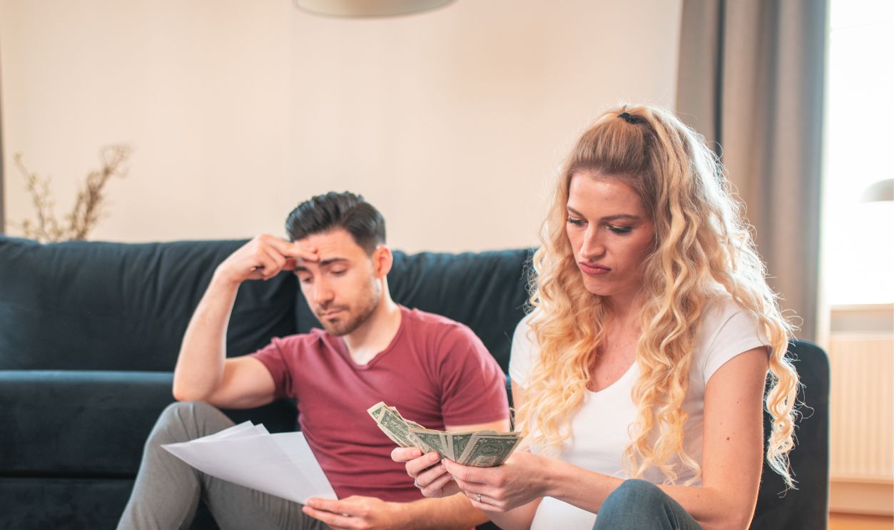 Young caucasian married couple discussing their finances al home. They are counting money and looking stressed.