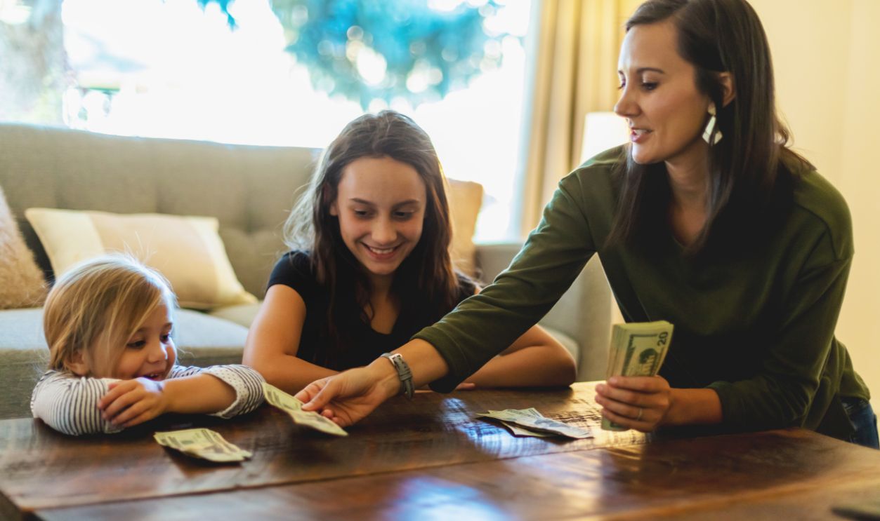 In Western Colorado Millennial Female Mother with Teenage and Pre School Age Daughters Handling and Counting Money and Passing Our Allowances Training How to budget and be good stewards of resources