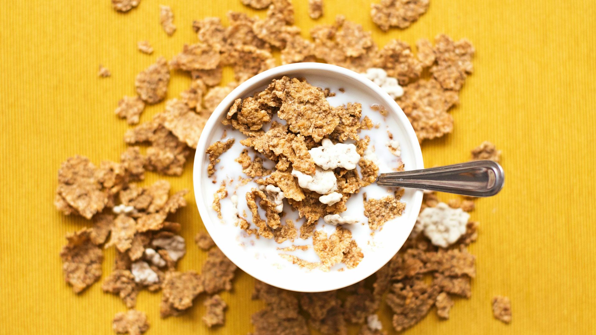top view of corn flakes in bowl with milk and silver spoon