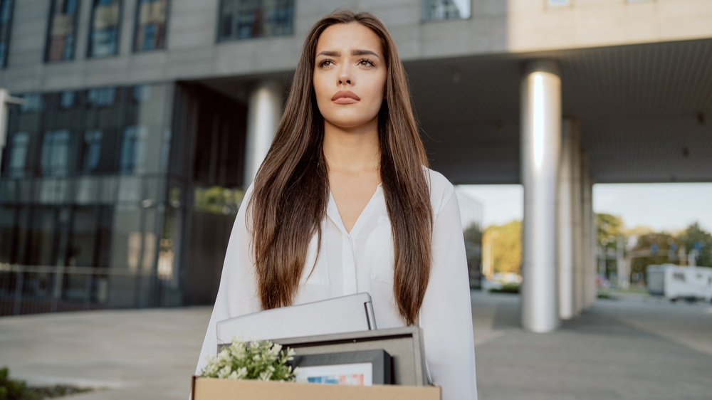 Sad woman in front of office building with belongings just quit job or is fired