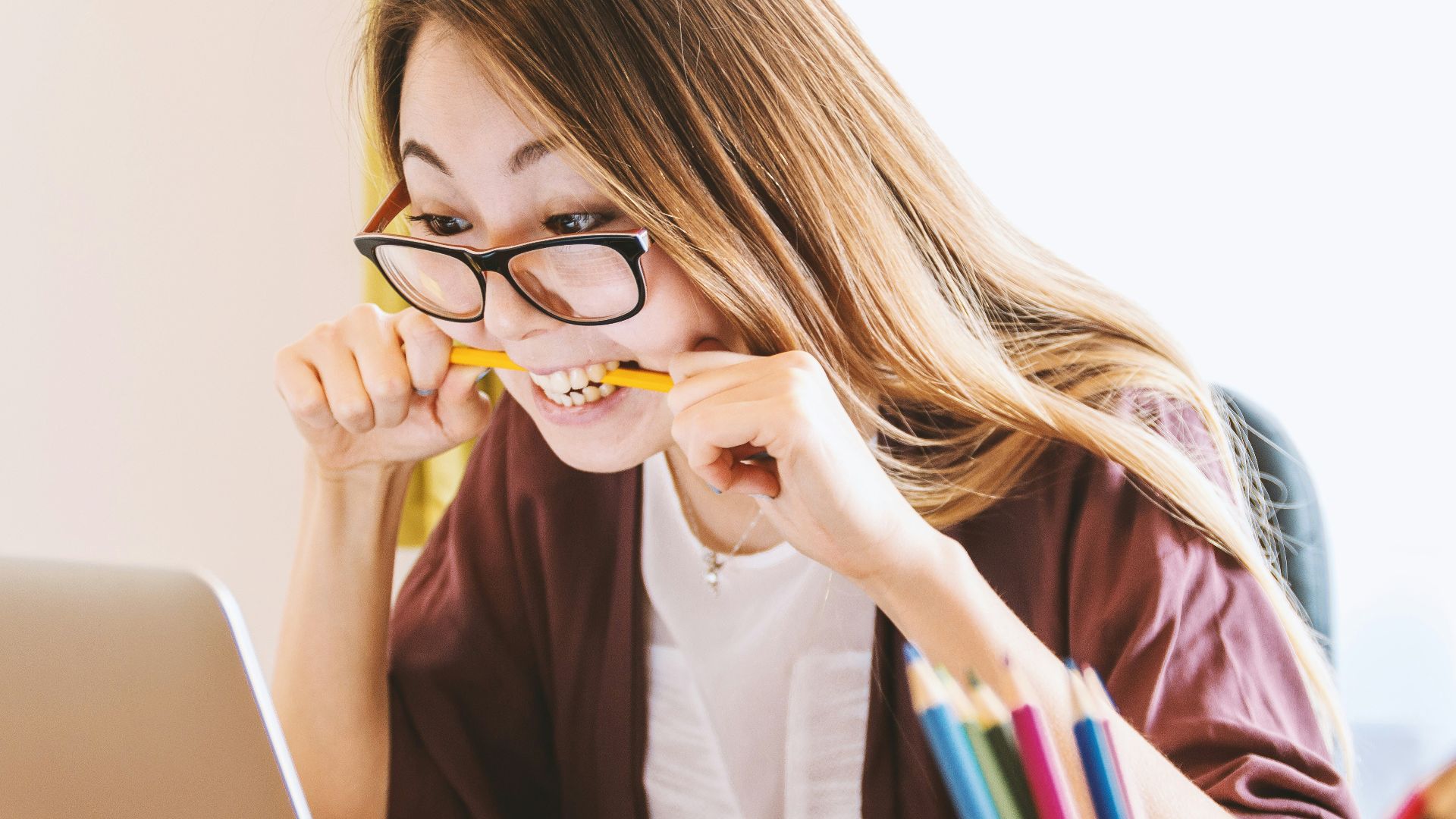 woman biting pencil while sitting on chair in front of computer during daytime