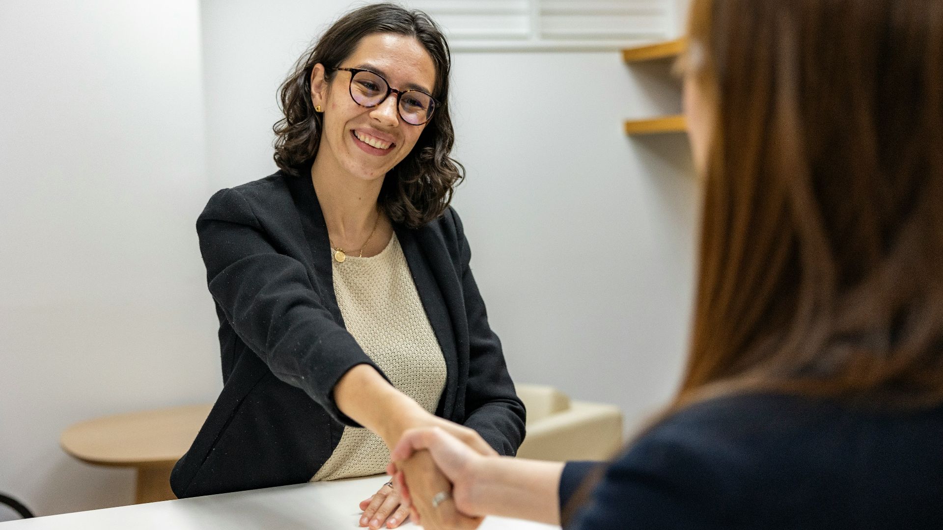 a woman shaking hands with another woman sitting at a table