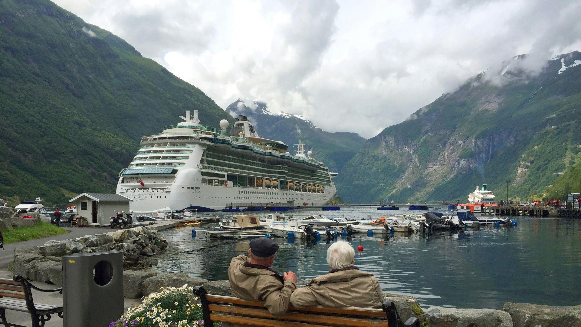 woman in brown coat sitting on brown wooden bench near white cruise ship during daytime