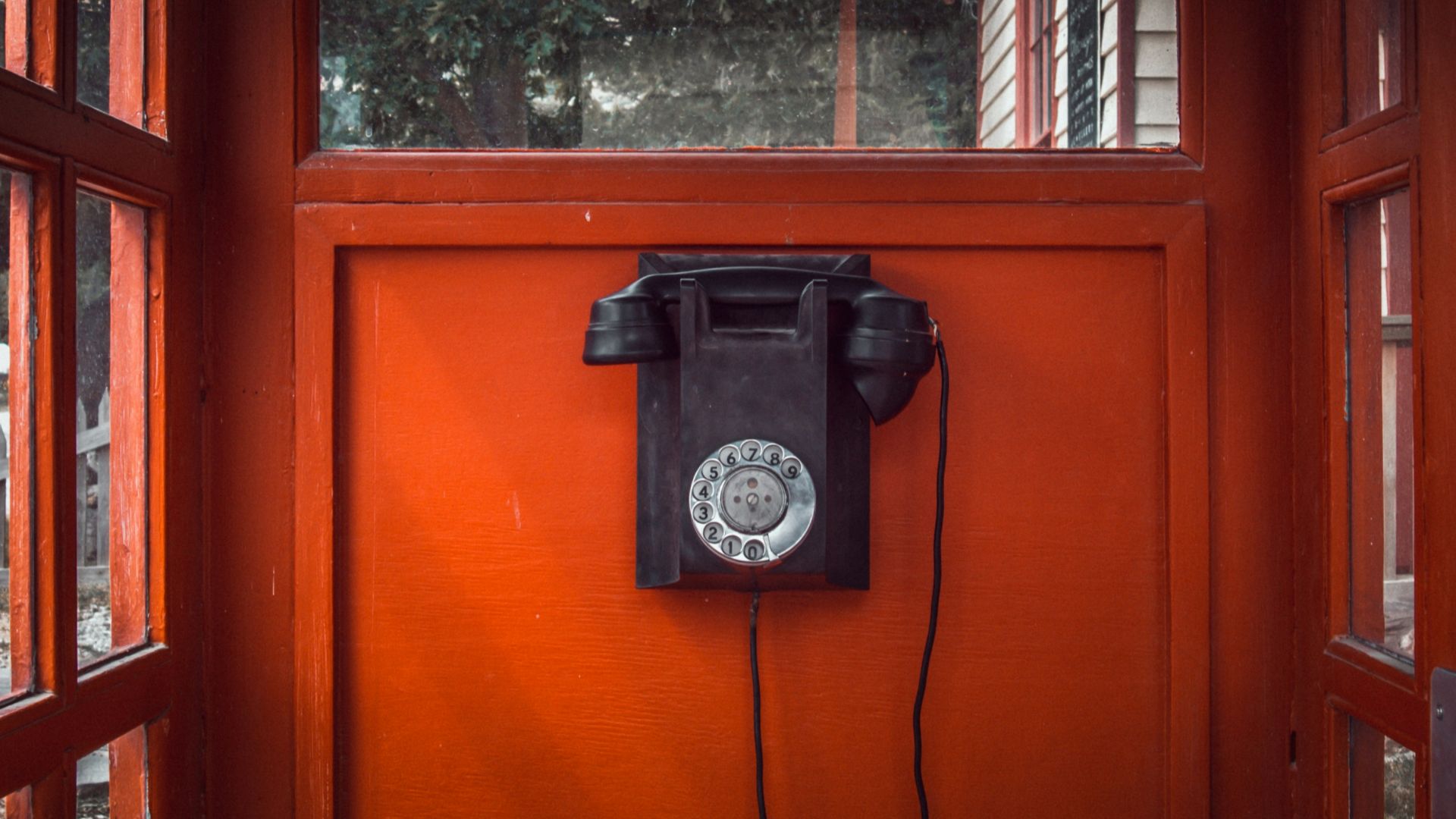 black rotary telephone mounted on red wooden wall