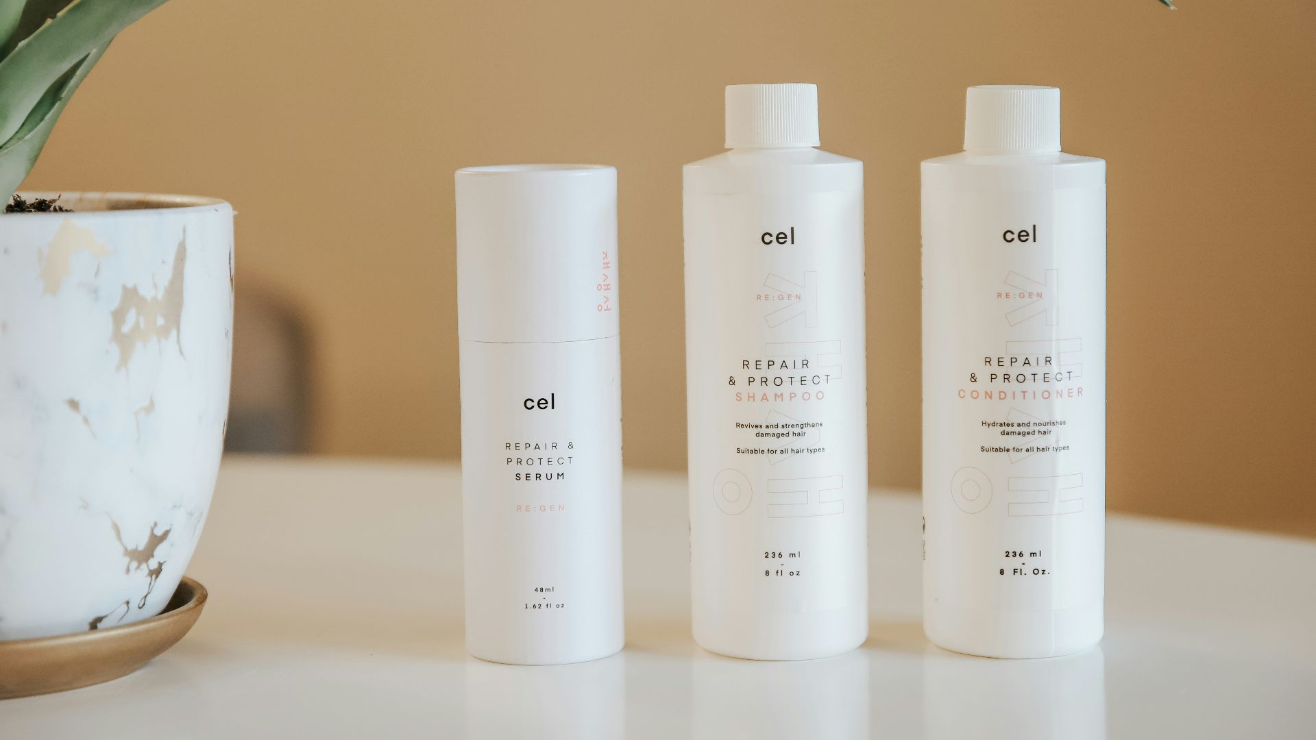 three bottles of lotion sitting on a table next to a potted plant