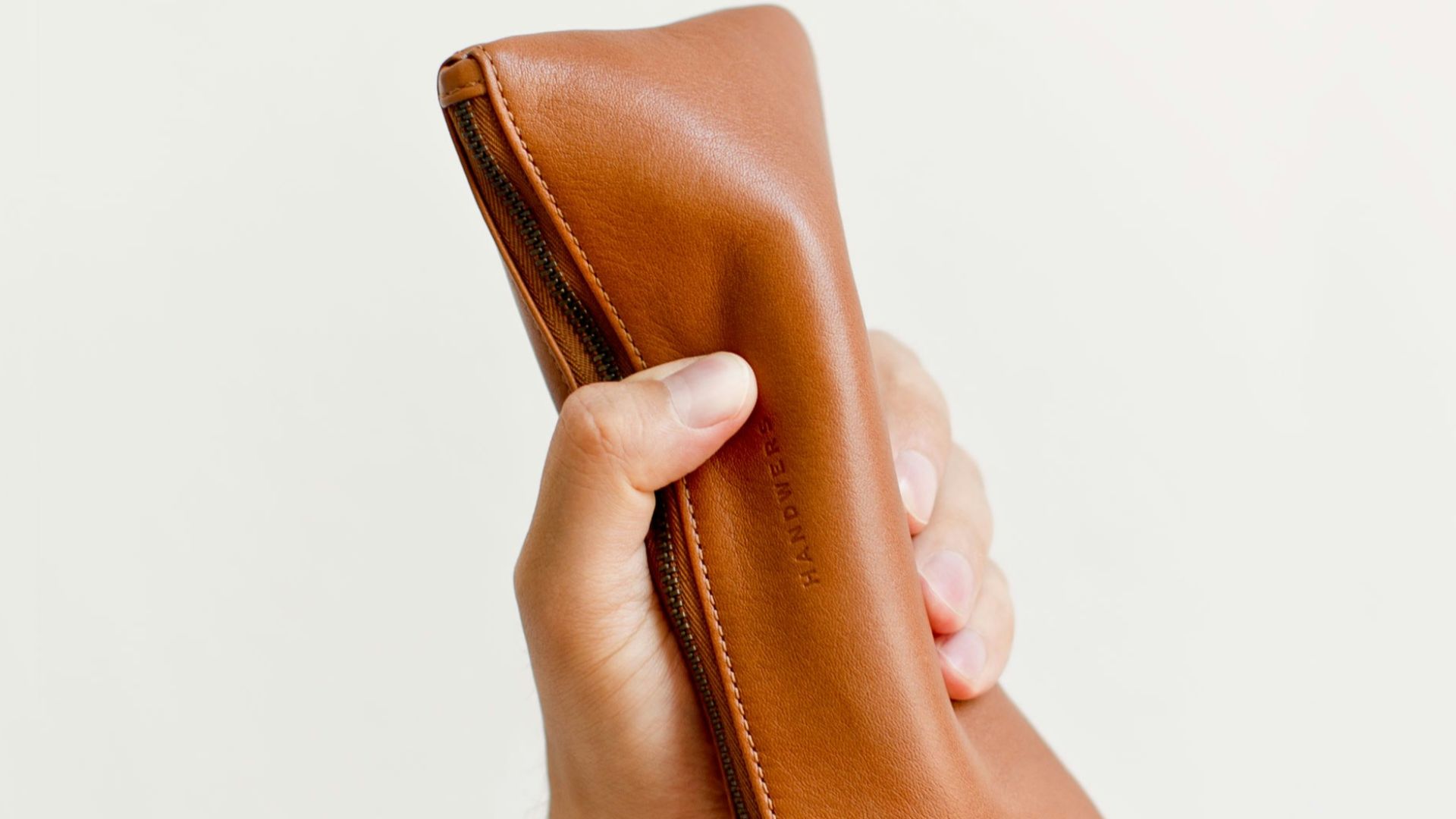 a hand holding a brown leather pouch
