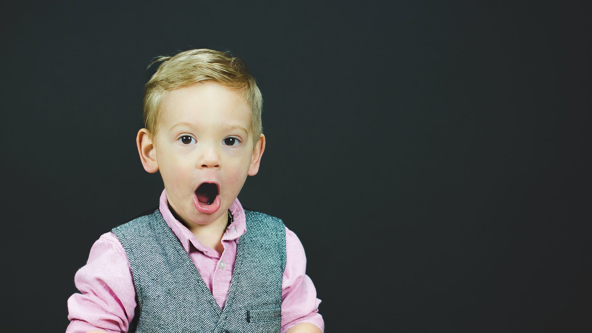 boy wearing gray vest and pink dress shirt holding book