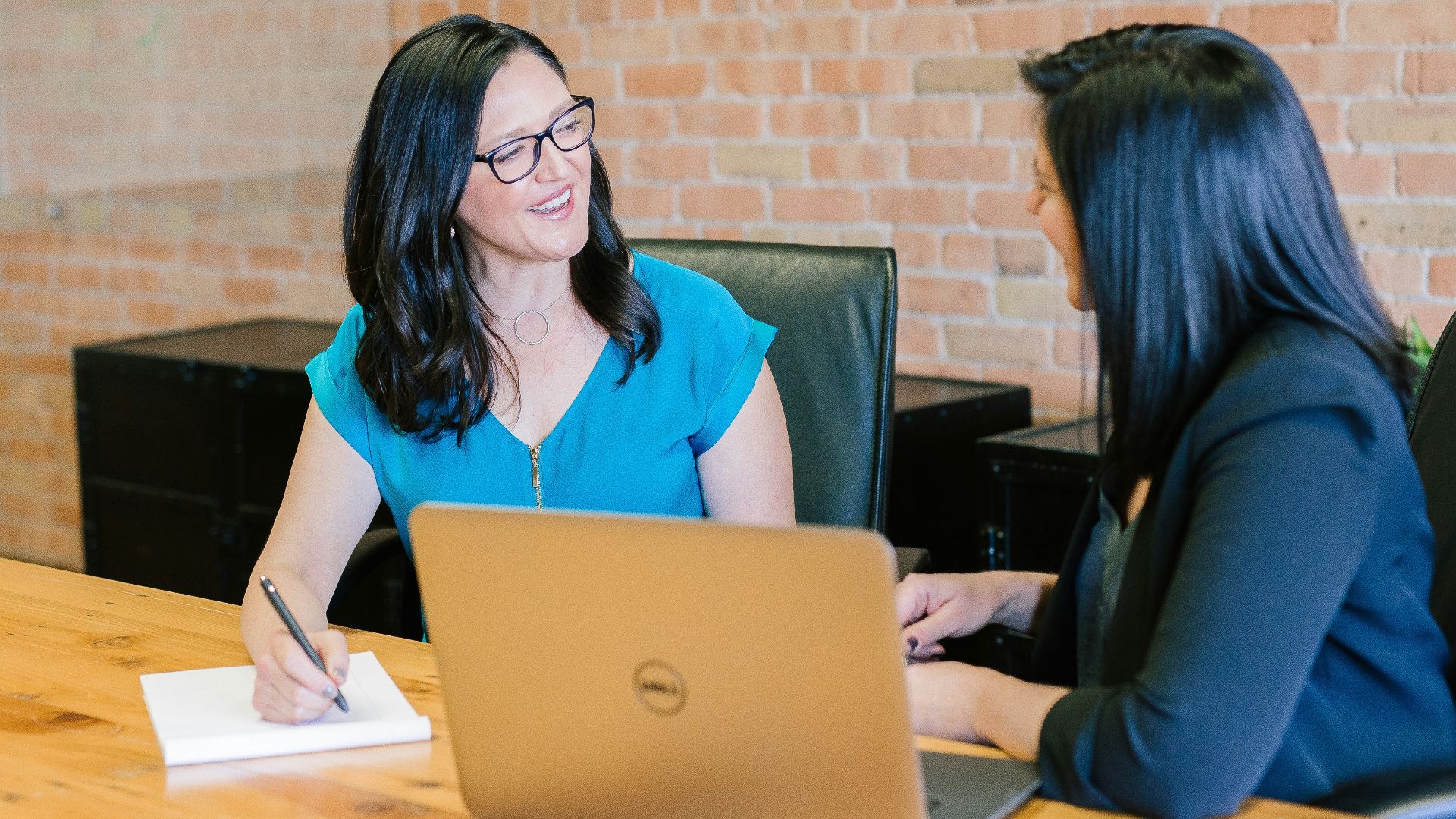 woman in teal t-shirt sitting beside woman in suit jacket
