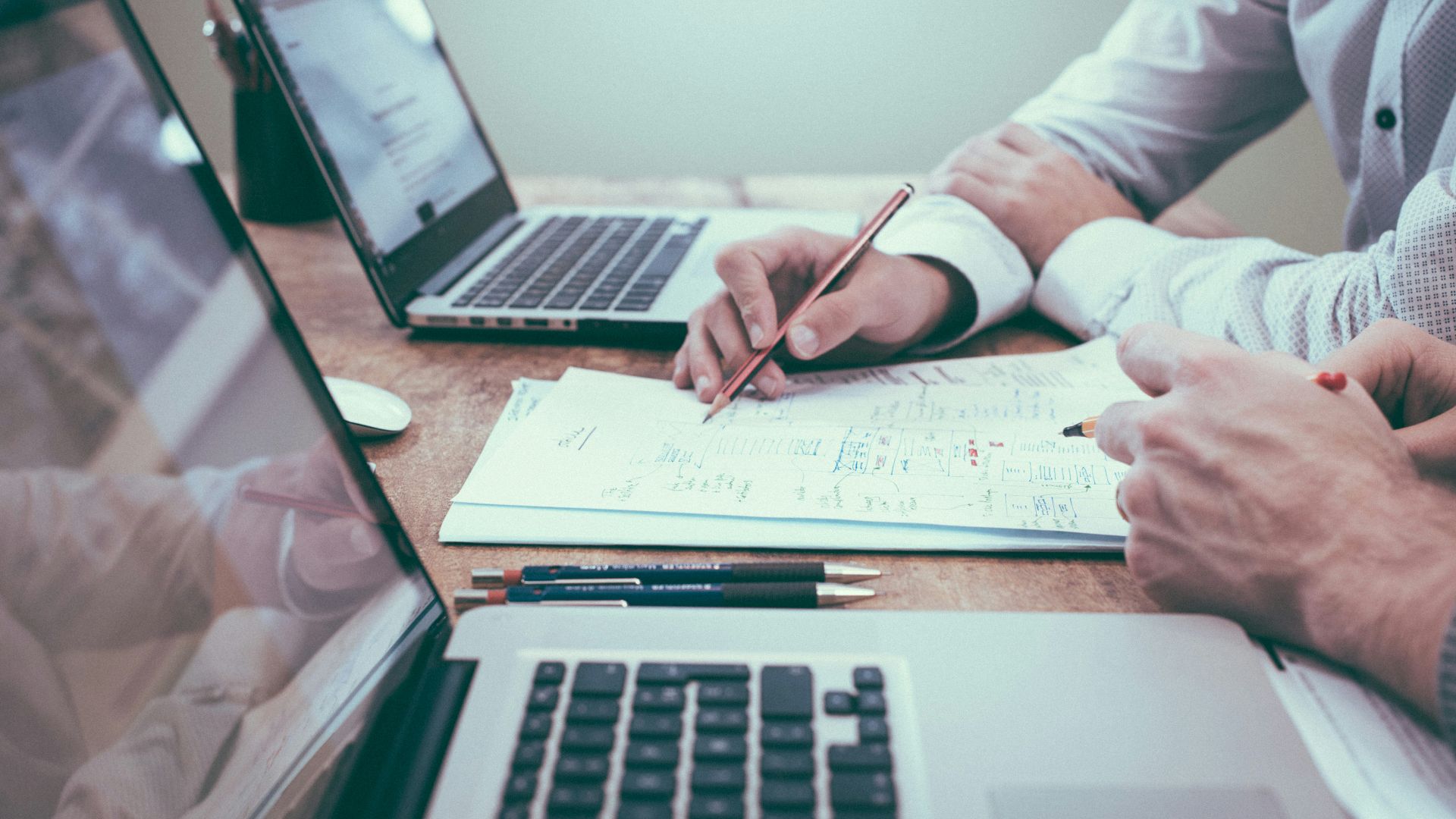 person holding pencil near laptop computer