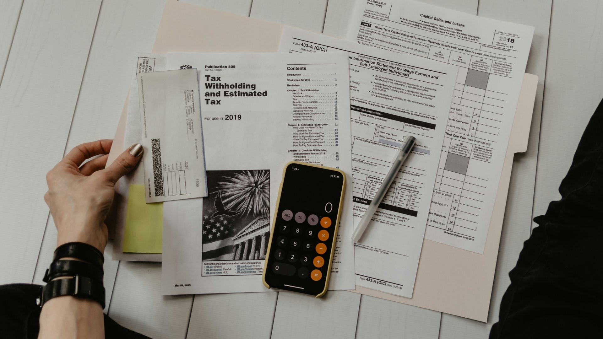 person holding paper near pen and calculator