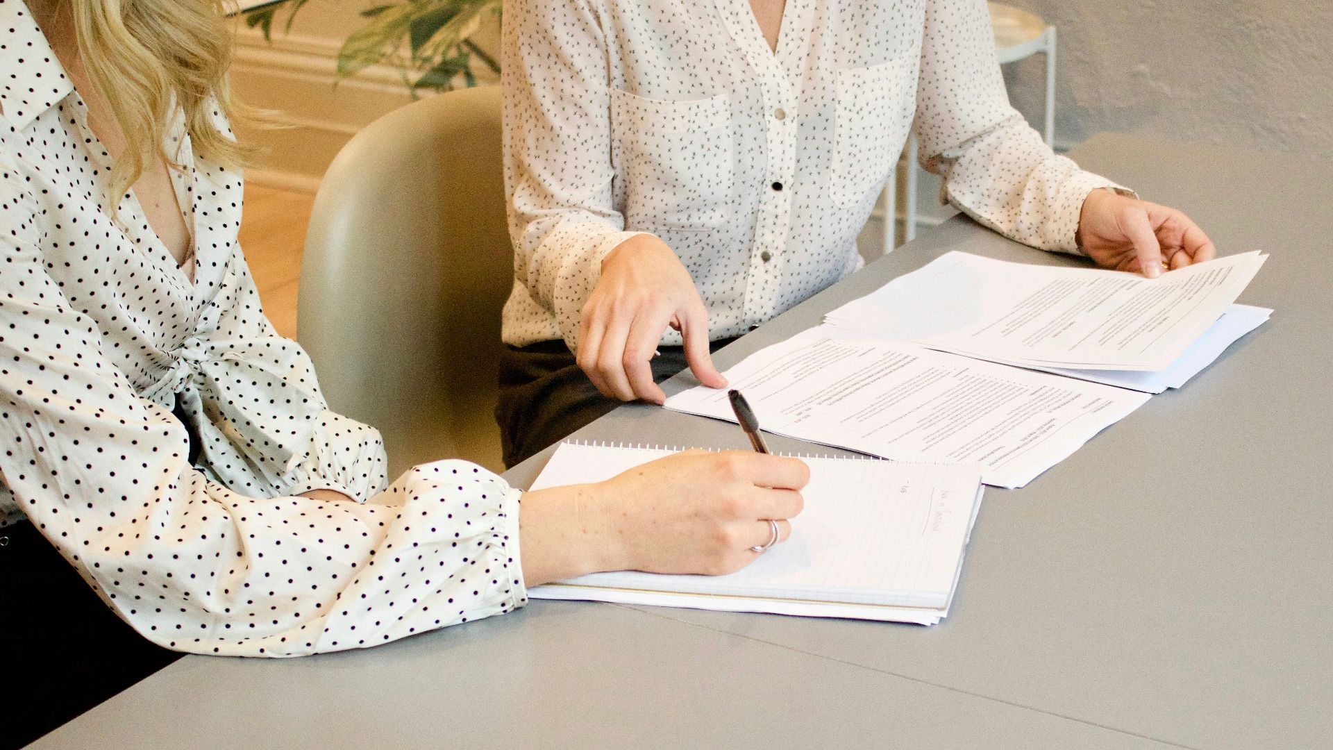 woman signing on white printer paper beside woman about to touch the documents