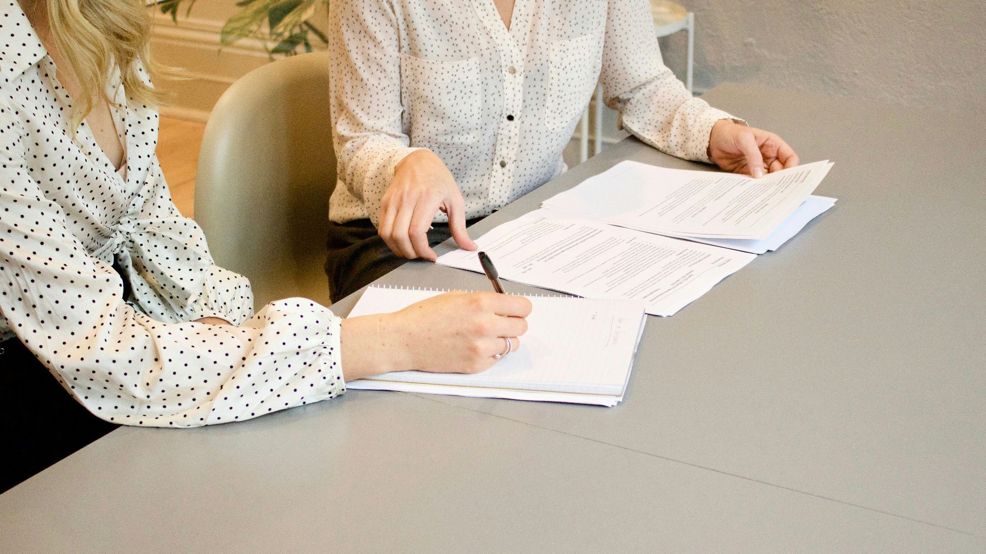 woman signing on white printer paper beside woman about to touch the documents
