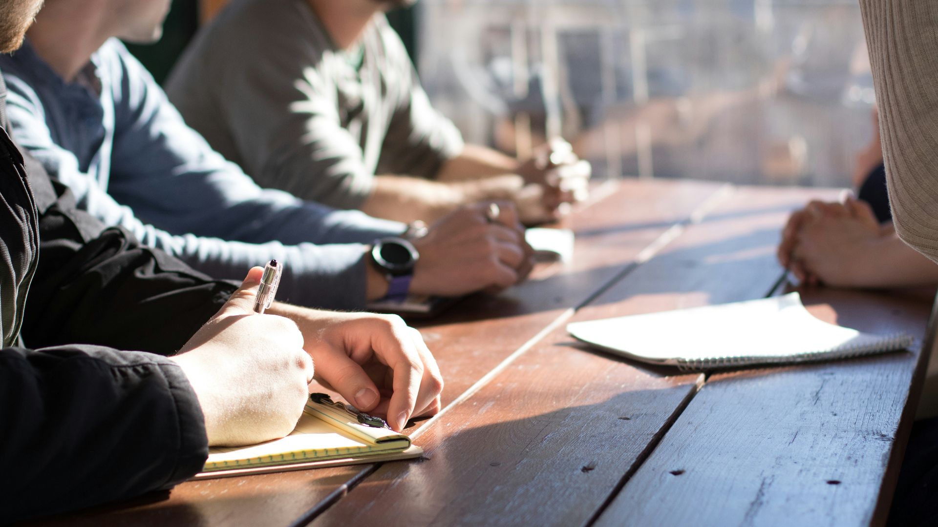 people sitting on chair in front of table while holding pens during daytime