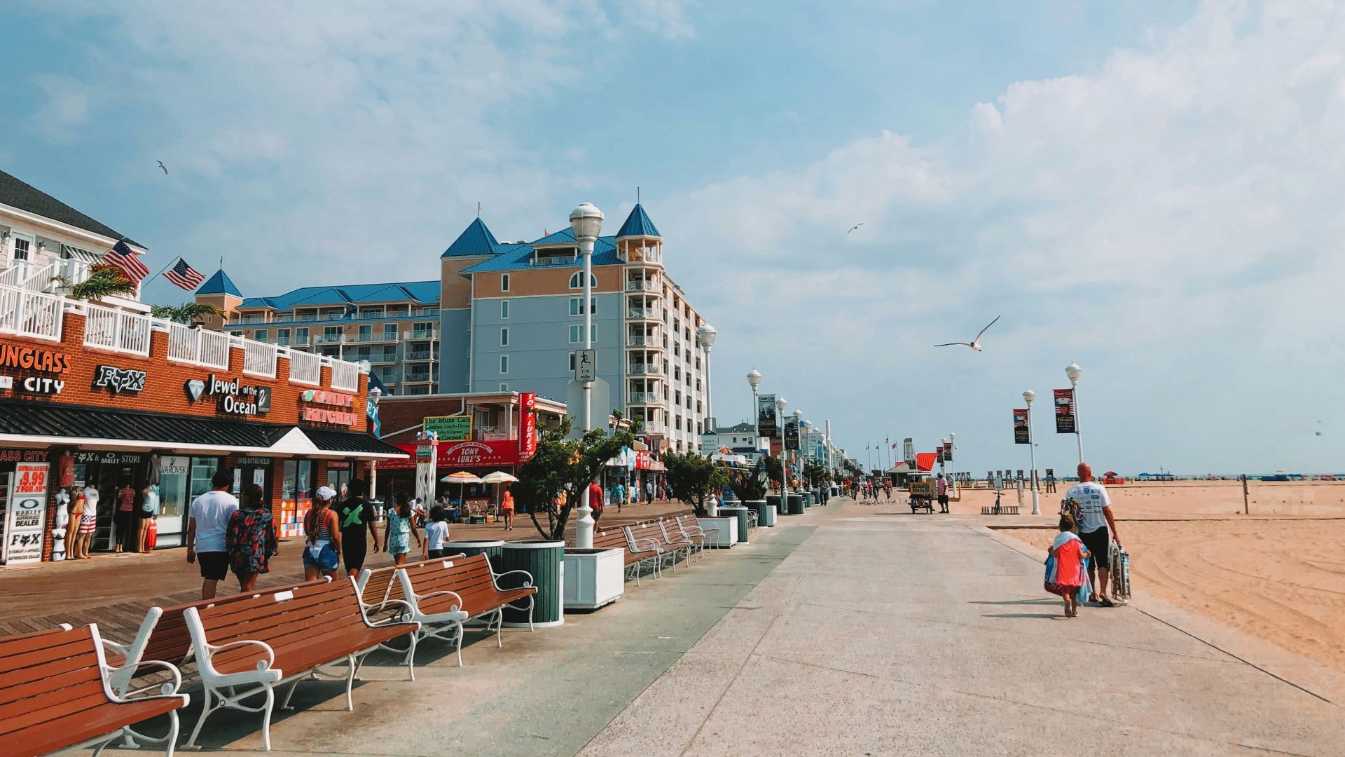 people walking on boardwalk near buildings under white and blue sky