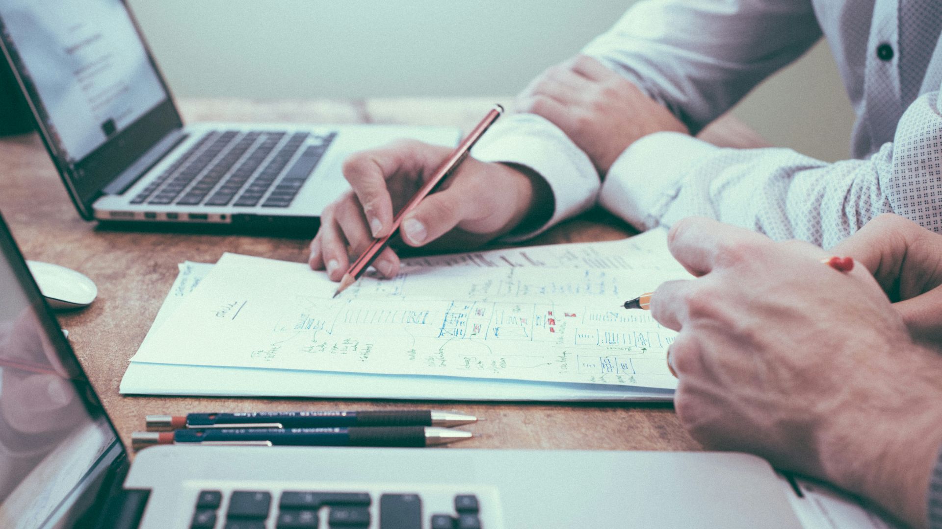 person holding pencil near laptop computer