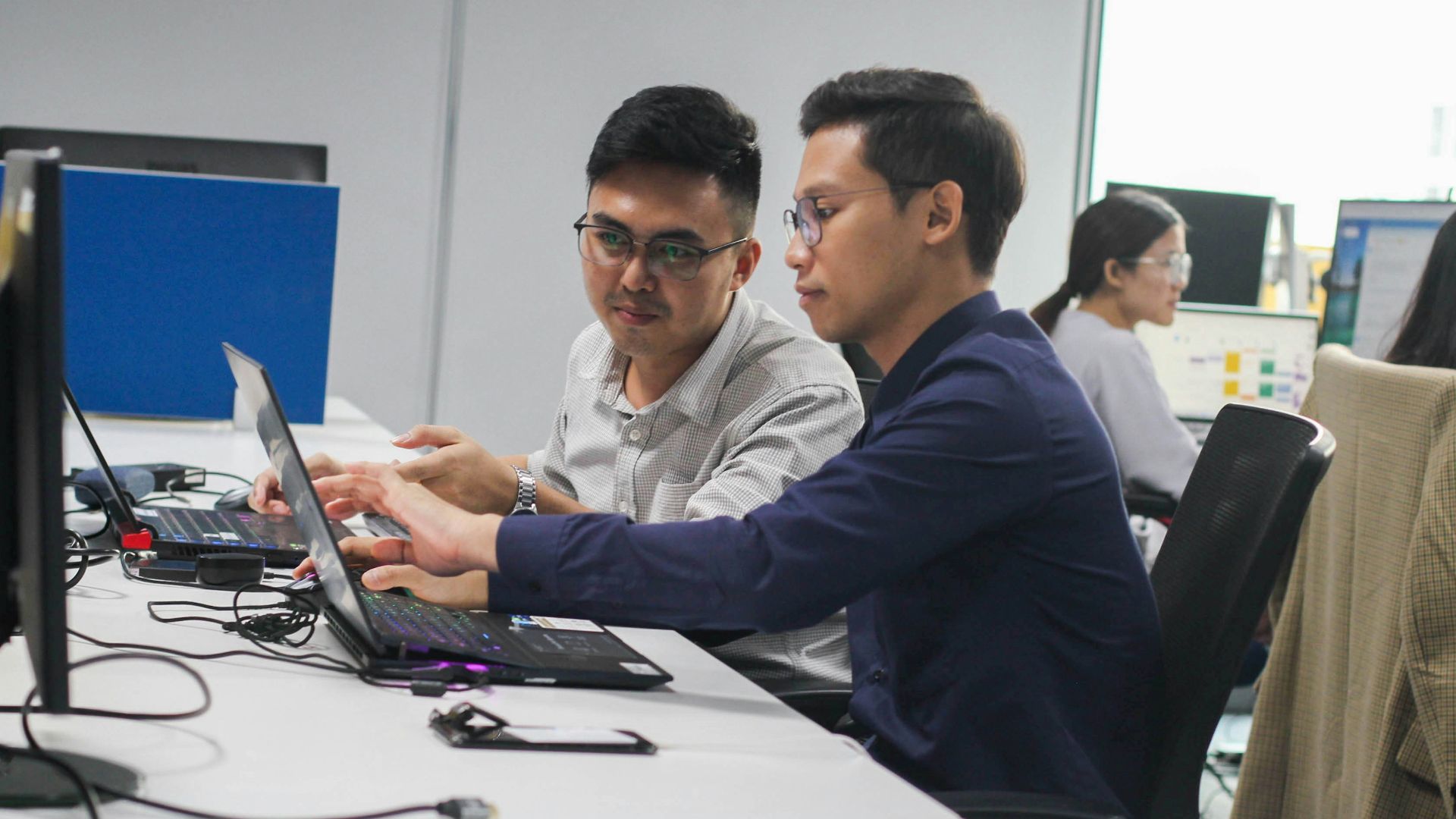 two men sitting at a desk looking at a laptop