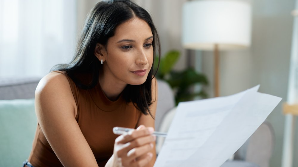 Woman, documents and reading on sofa checking bills