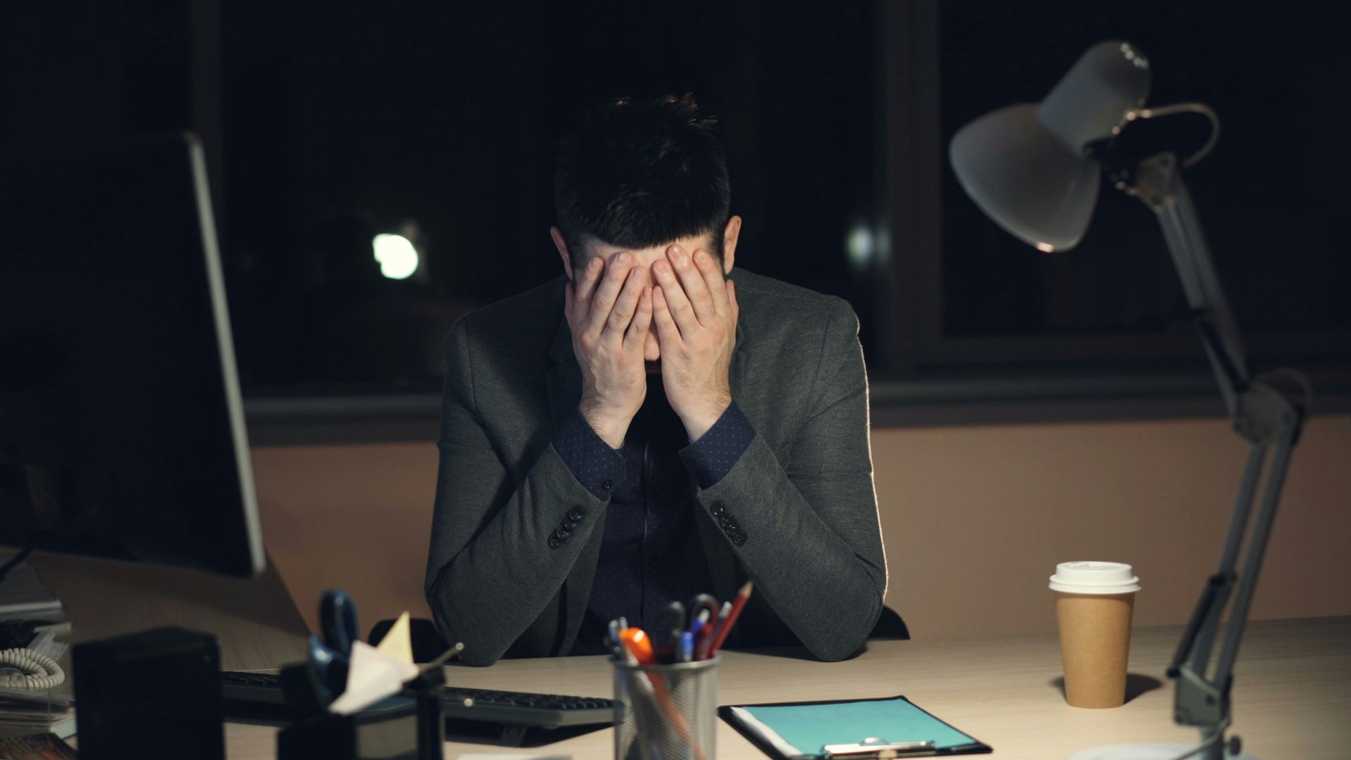 Man in suit sits at desk, head in hands.