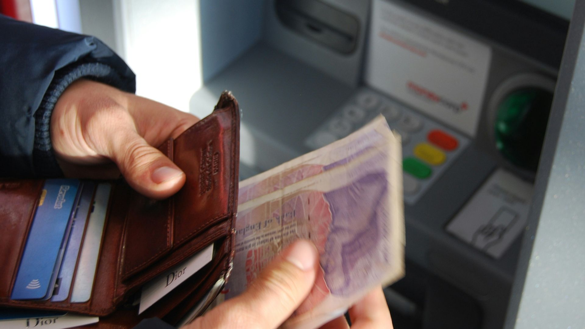 person holding brown leather wallet and banknotes