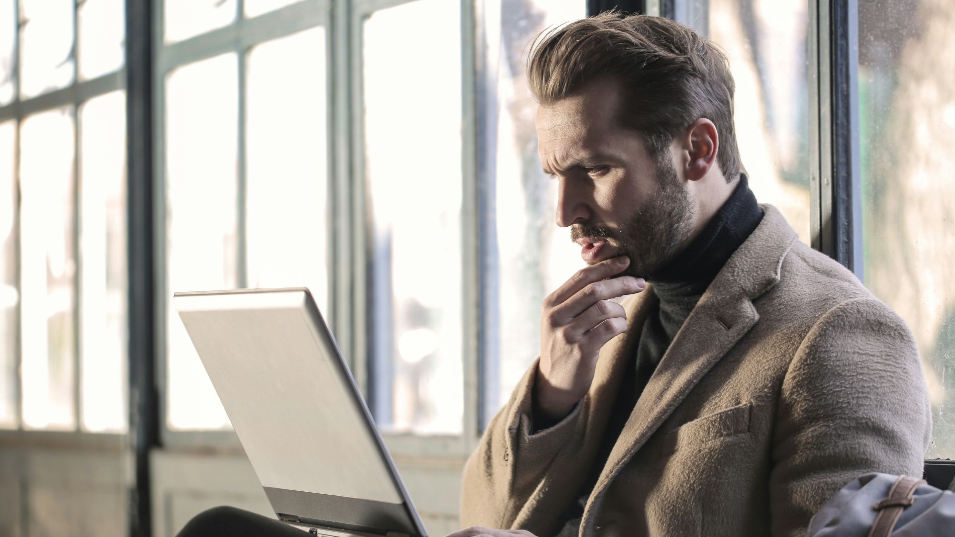 man holding his chin facing laptop computer