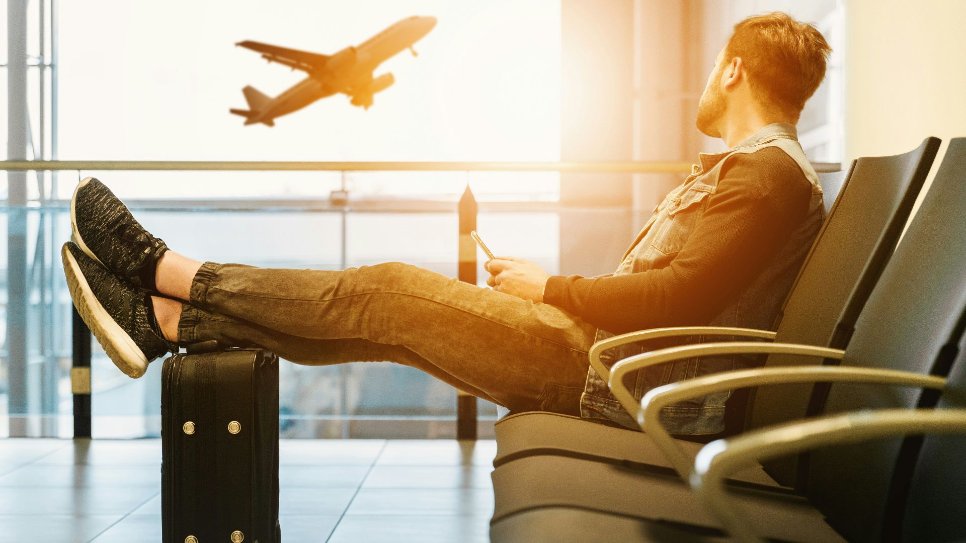 man sitting on gang chair with feet on luggage looking at airplane