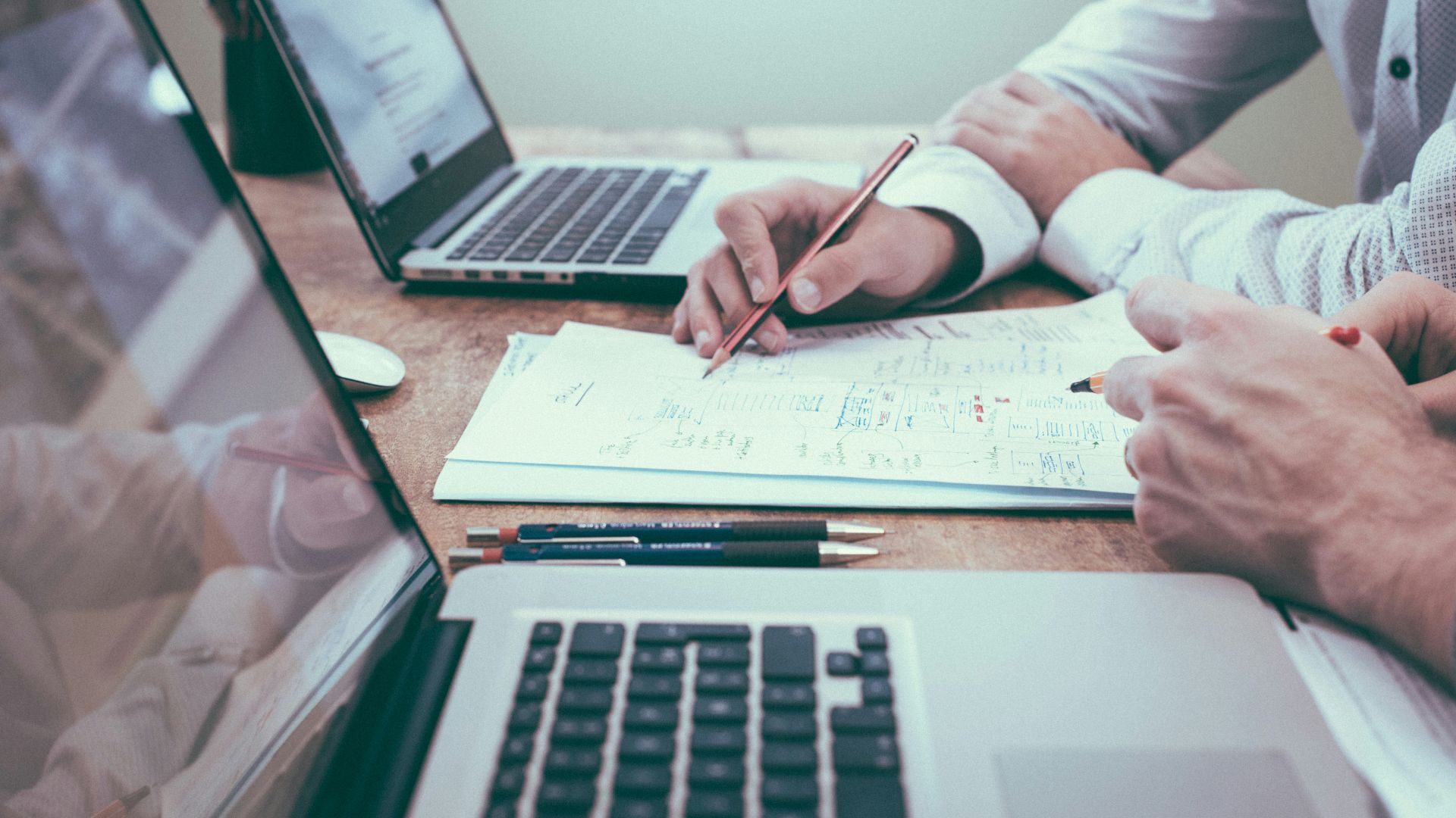 person holding pencil near laptop computer