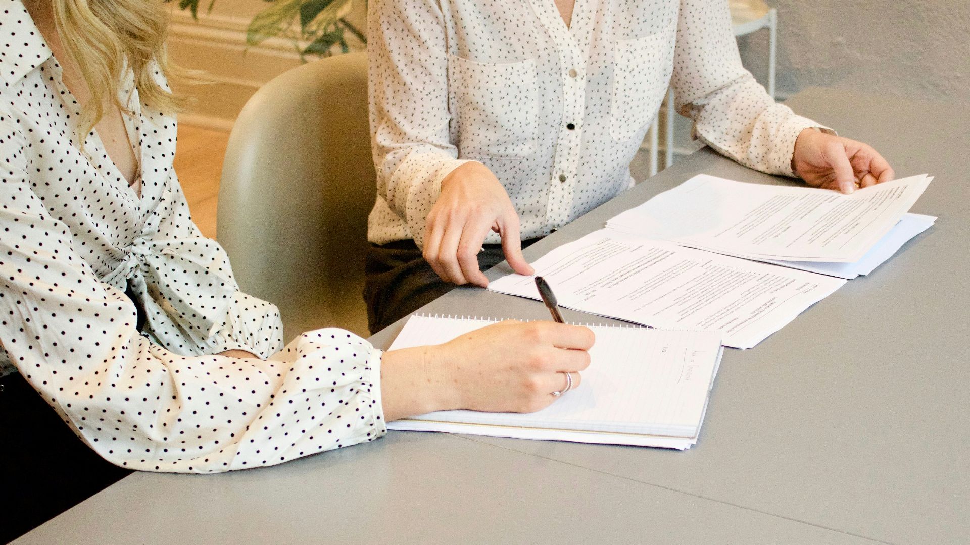 woman signing on white printer paper beside woman about to touch the documents