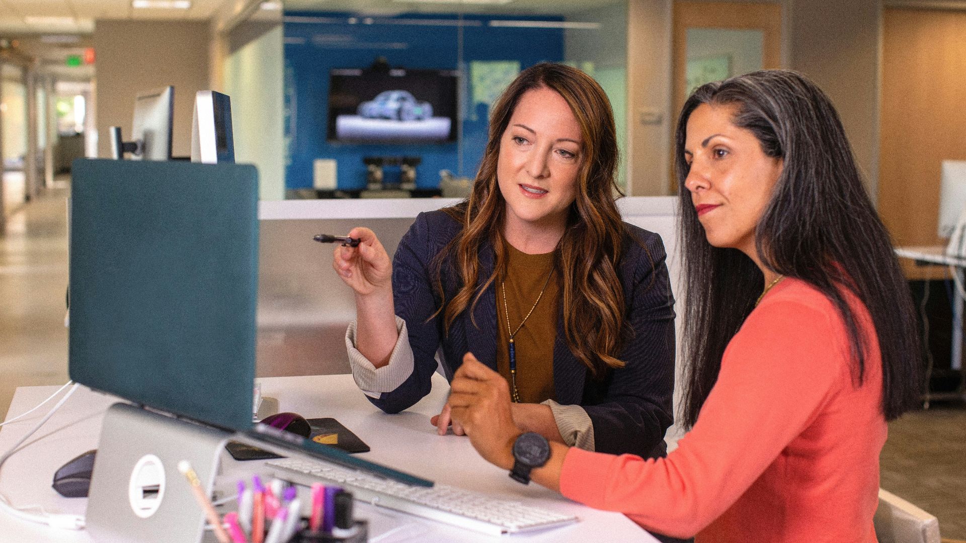 two women sitting at a table looking at a computer screen