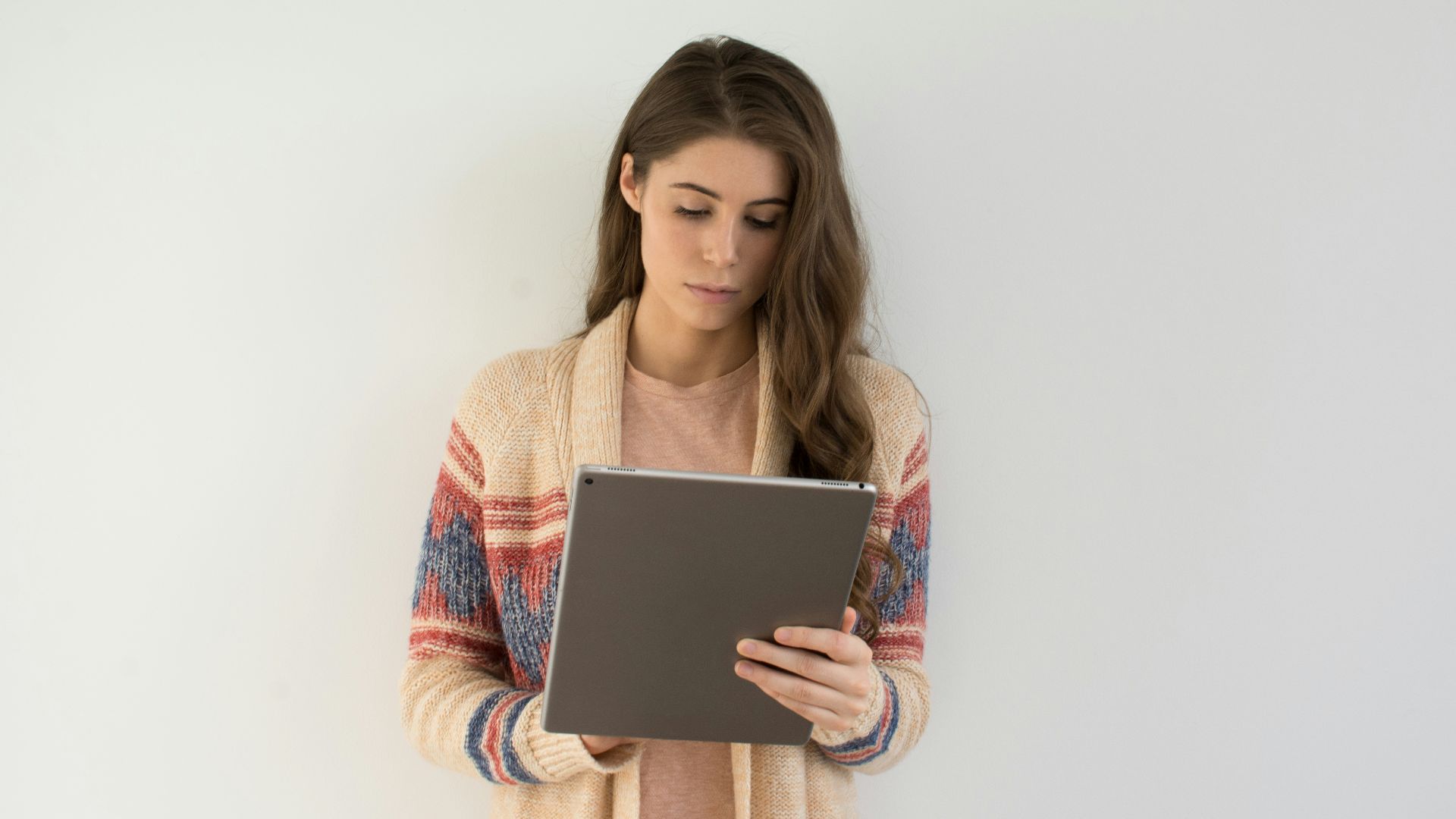 woman in beige, gray, and red sweater holding silver tablet computer