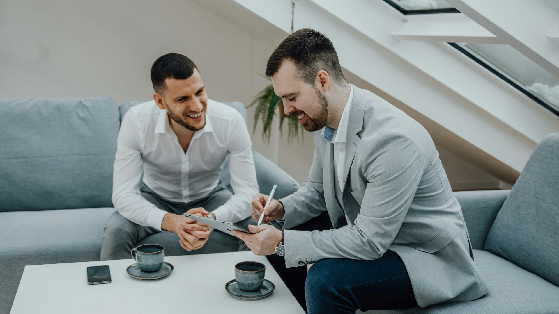 two men sitting on a couch signing something