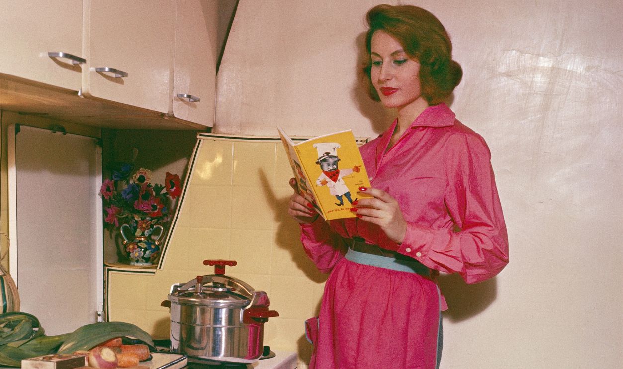 A Housewife In Her Kitchen Amenagee Consults His Cookbook Did With Her Pressure Cooker In 1961