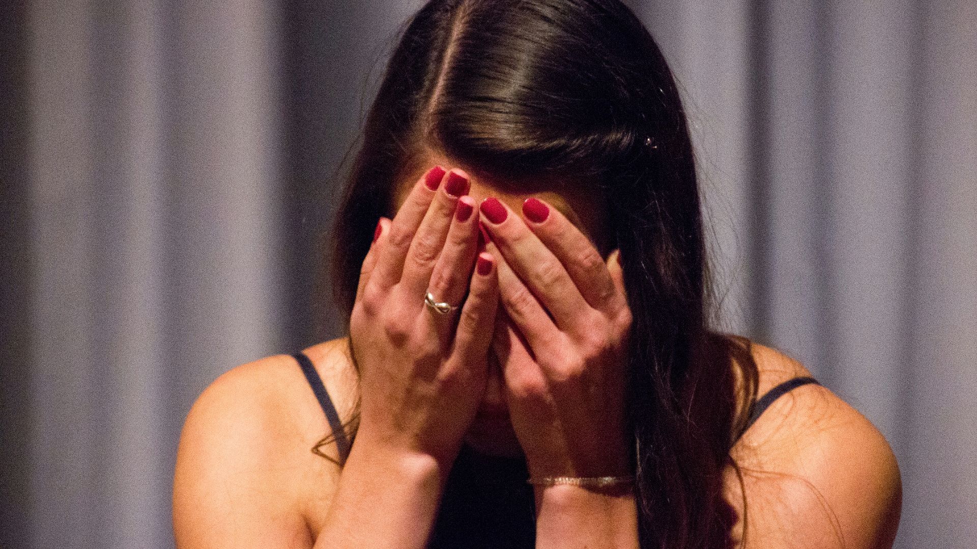 woman in black tank top covering her face with her hands