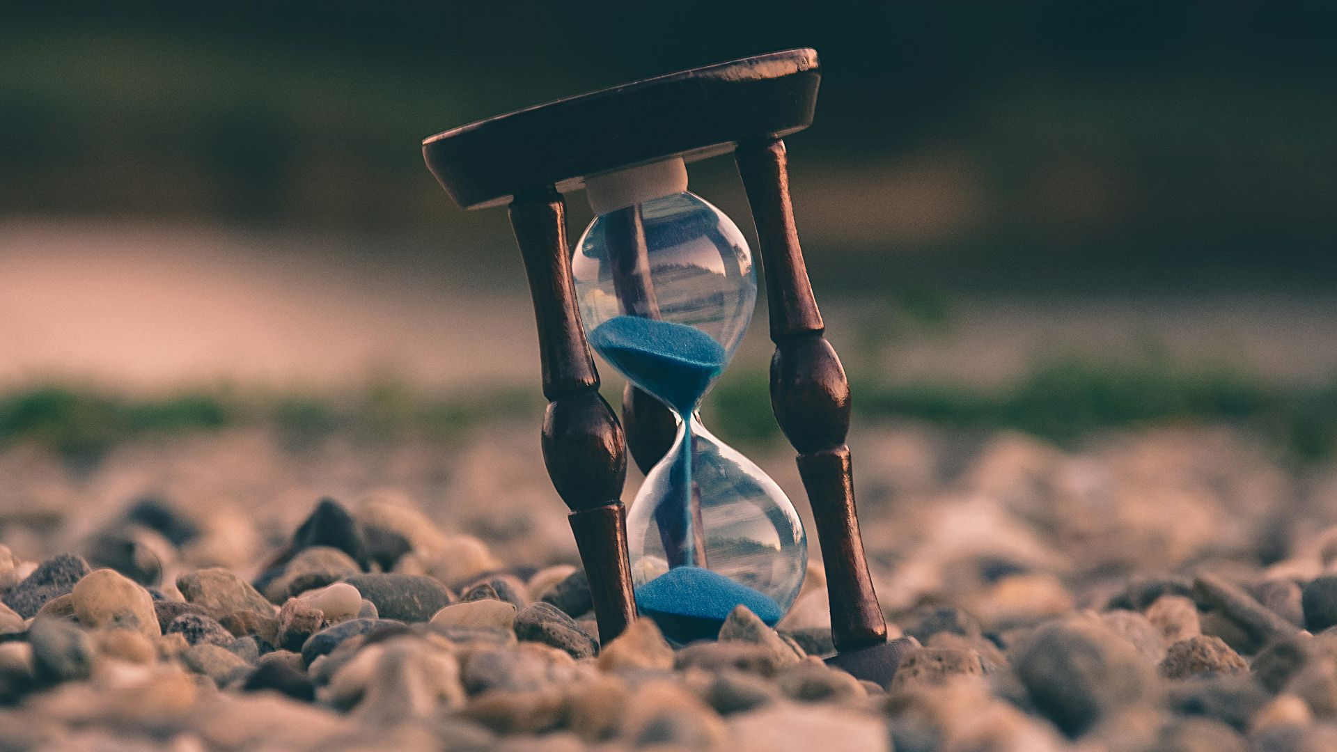 selective focus photo of brown and blue hourglass on stones