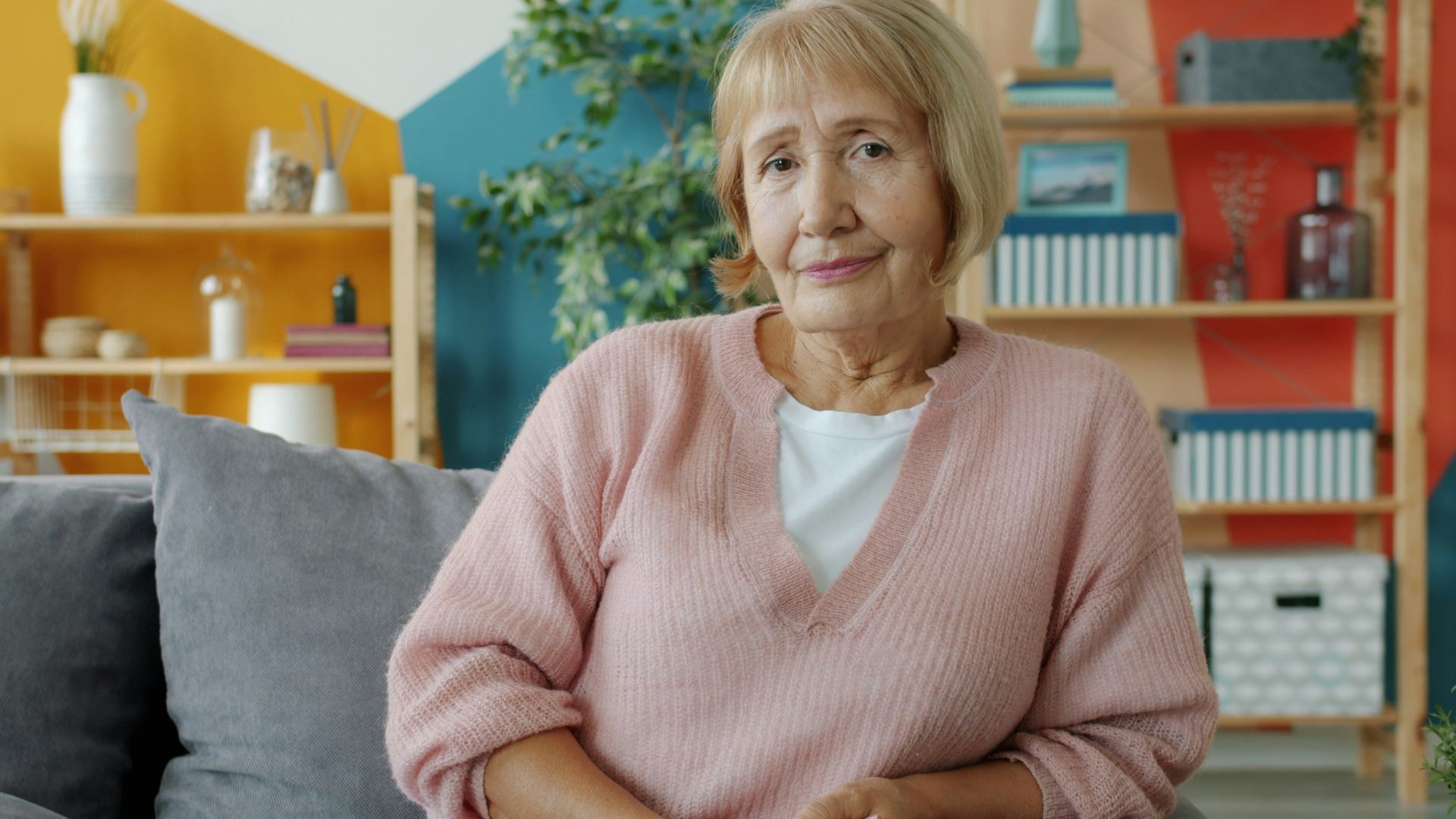 Elderly woman sitting on a couch in a colorful room.