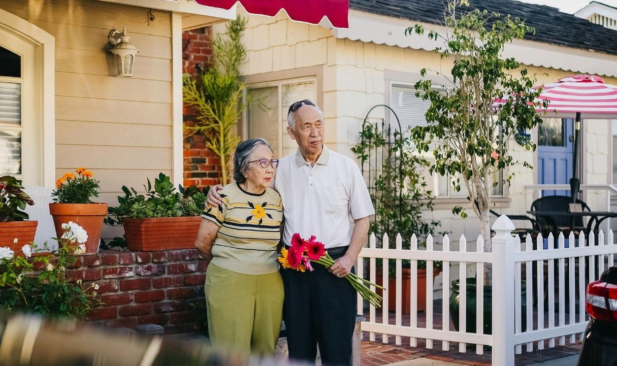 Elderly Couple Standing Outside the House