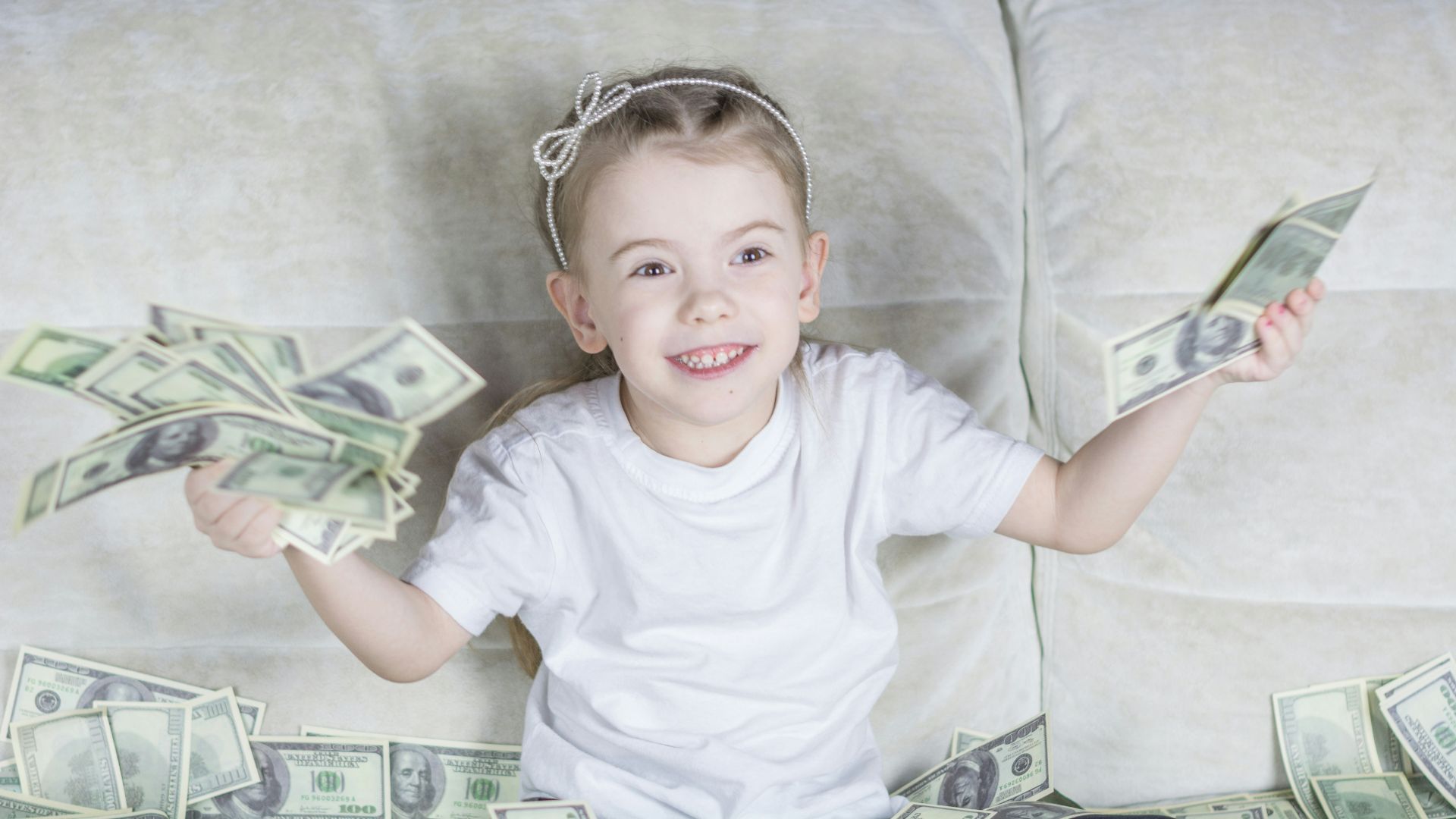a little girl sitting on a couch holding money
