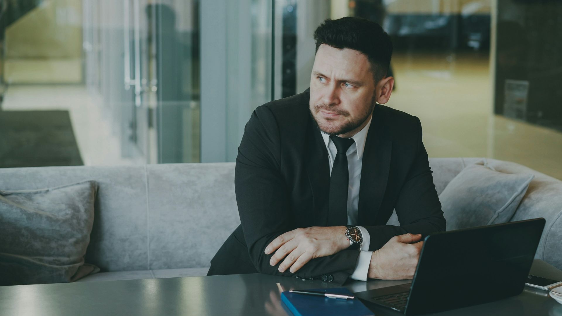 Man in suit sitting at table with laptop and coffee.