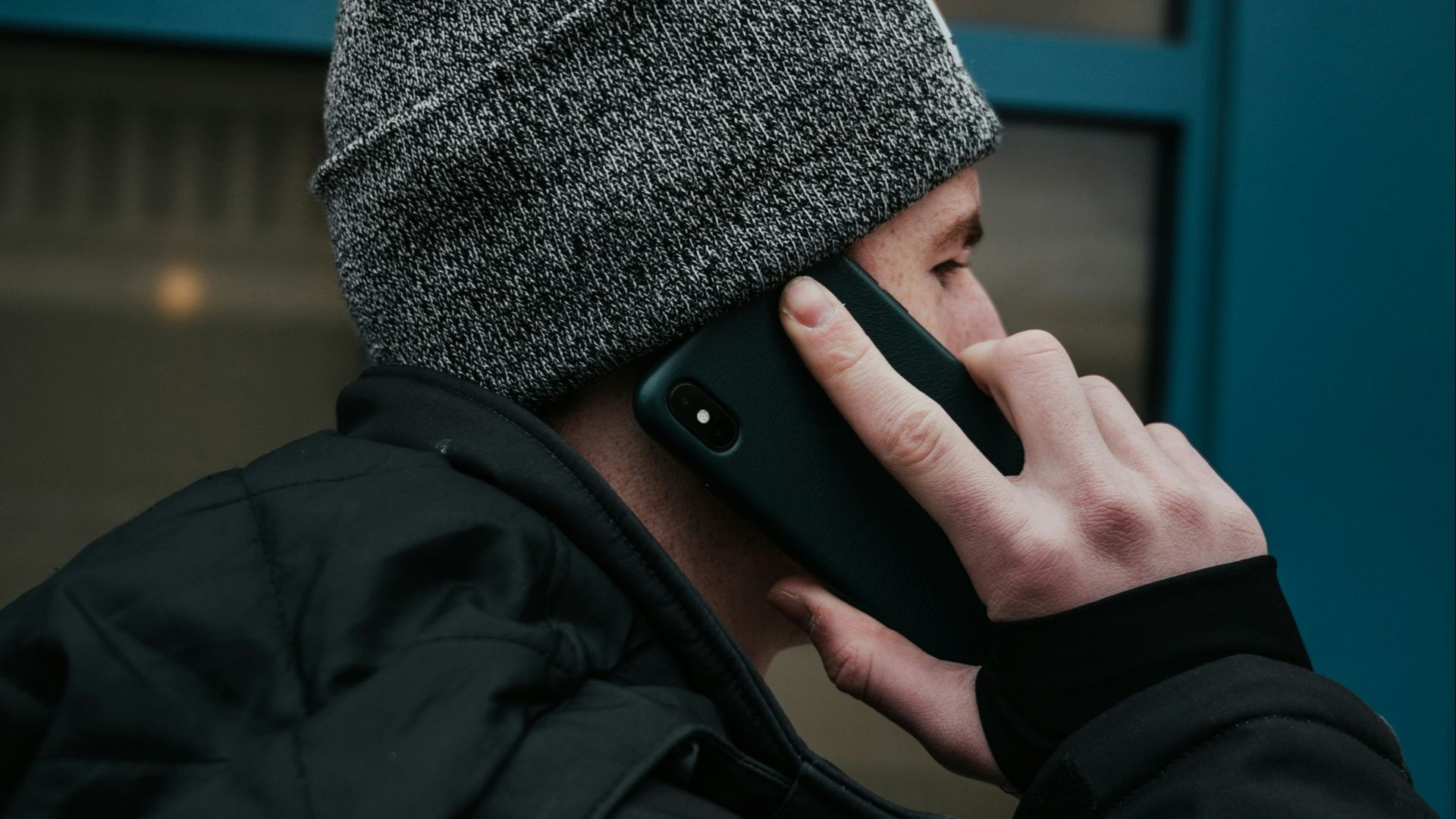 man in gray beanie hat and black jacket using smartphone