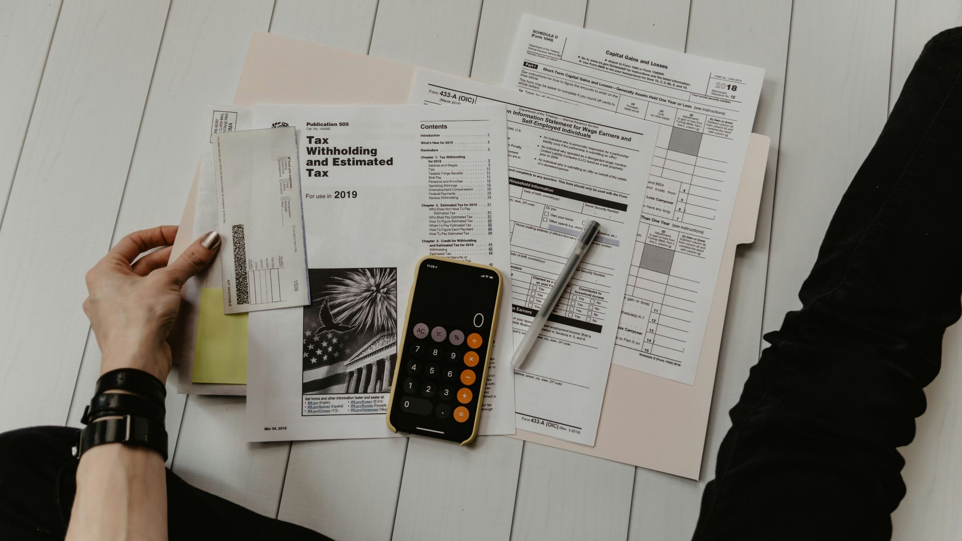 person holding paper near pen and calculator