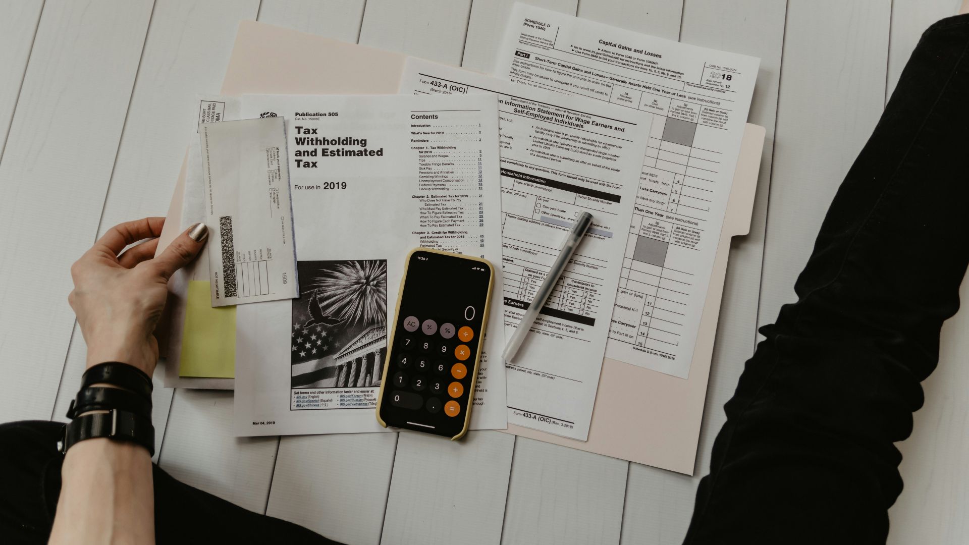 person holding paper near pen and calculator