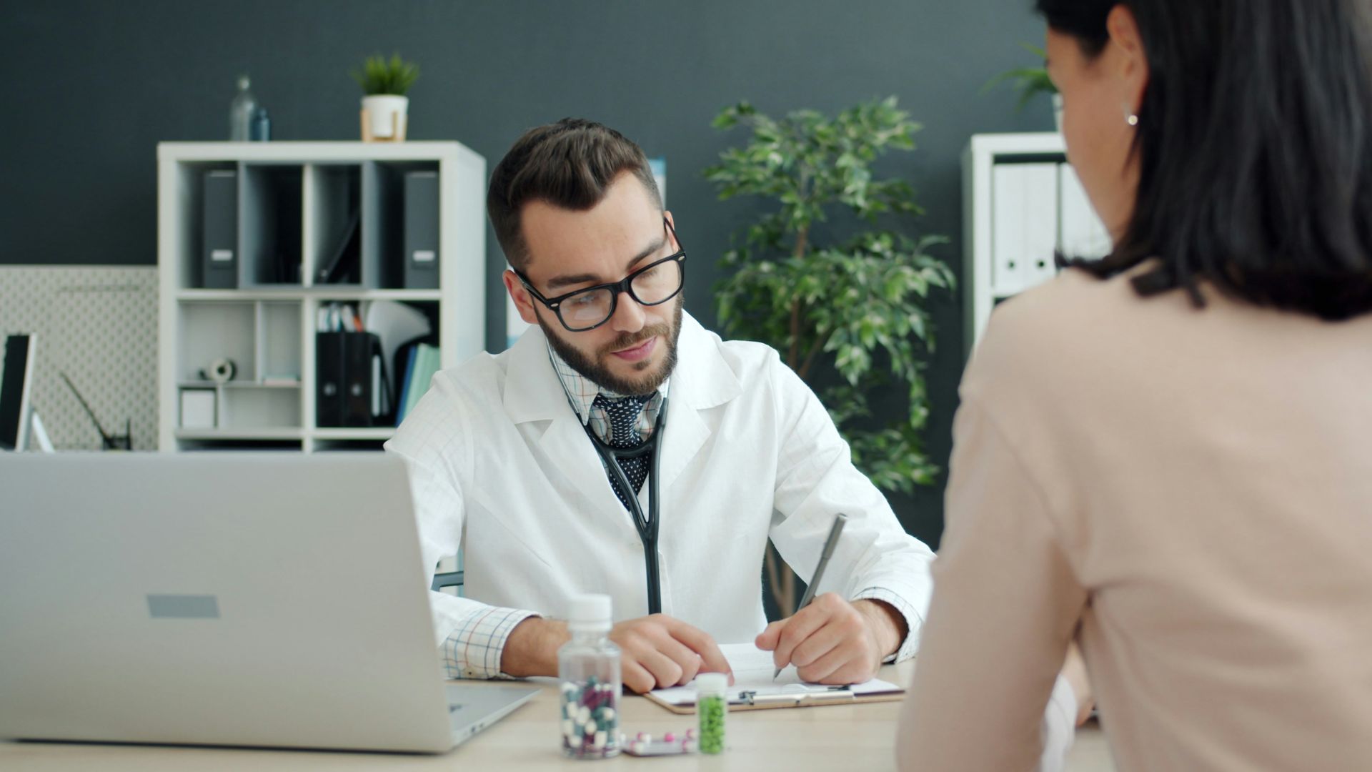Doctor writing notes while patient sits opposite.