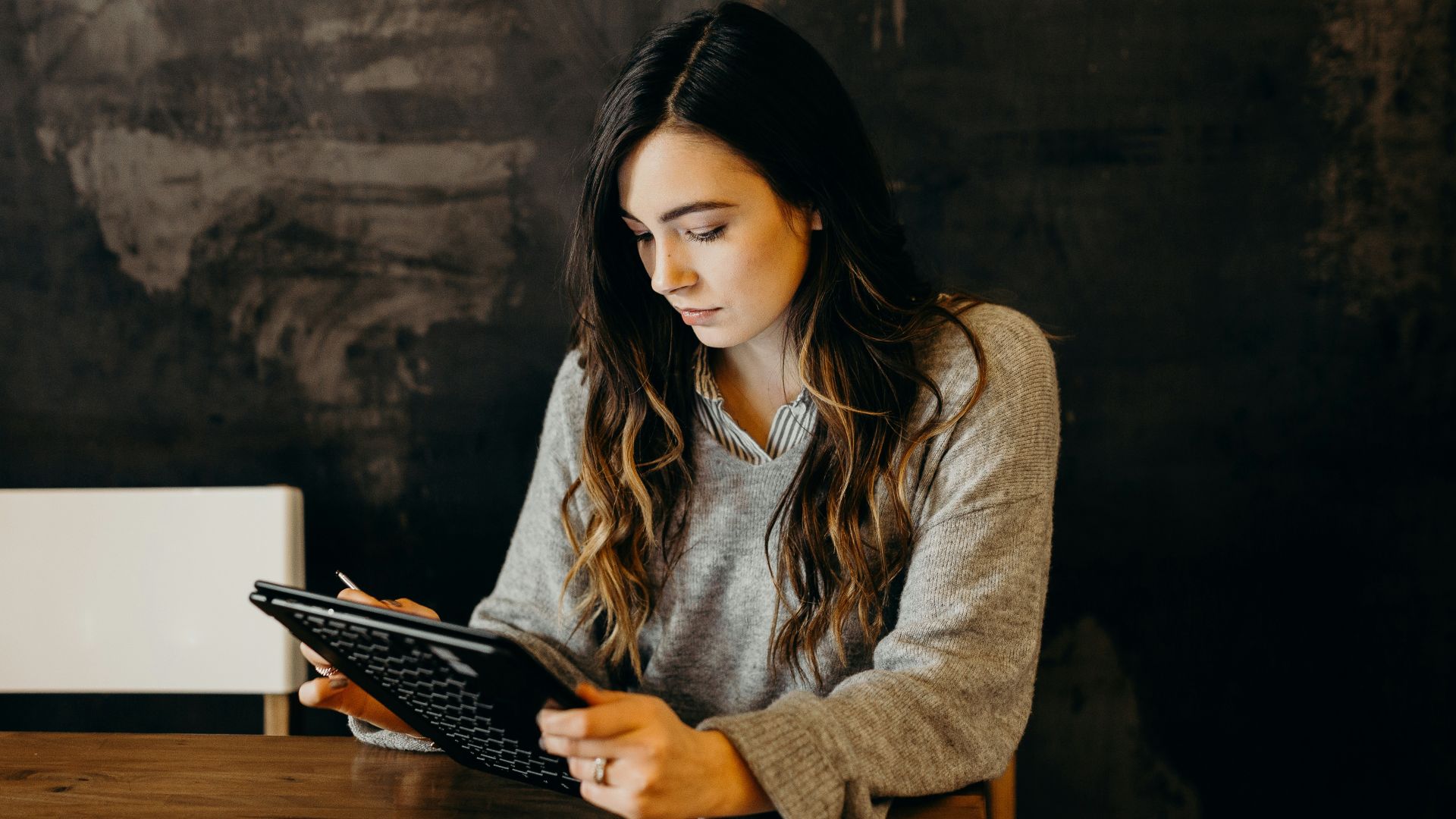 A woman in a grey sweater using a tablet at a wooden table