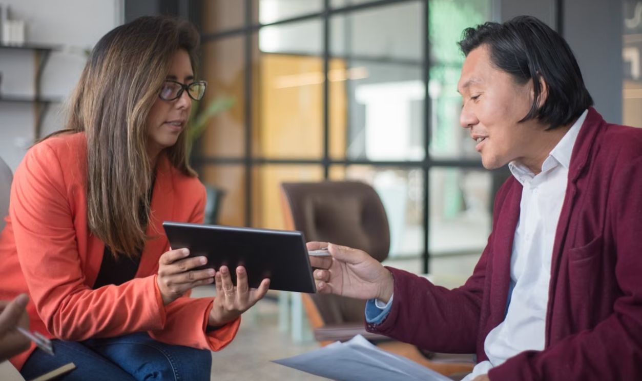 Two professionals discussing work with a tablet in a modern office environment.