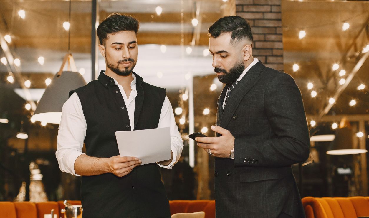 Two businessmen reviewing documents and smartphone in a restaurant setting