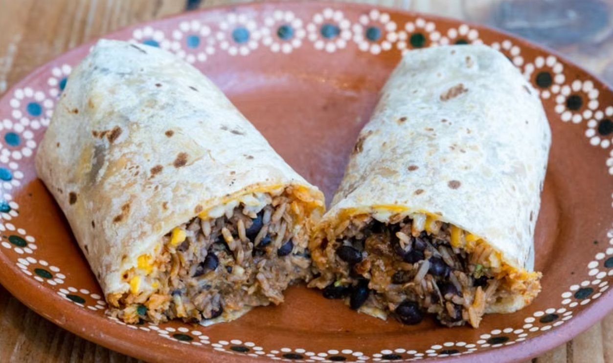 Tasty Mexican burrito split open to show filling on a rustic clay plate