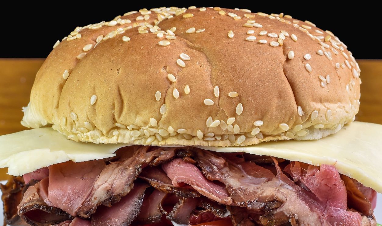 roast beef sandwich with tomatoes and swiss cheese on a sesame bun