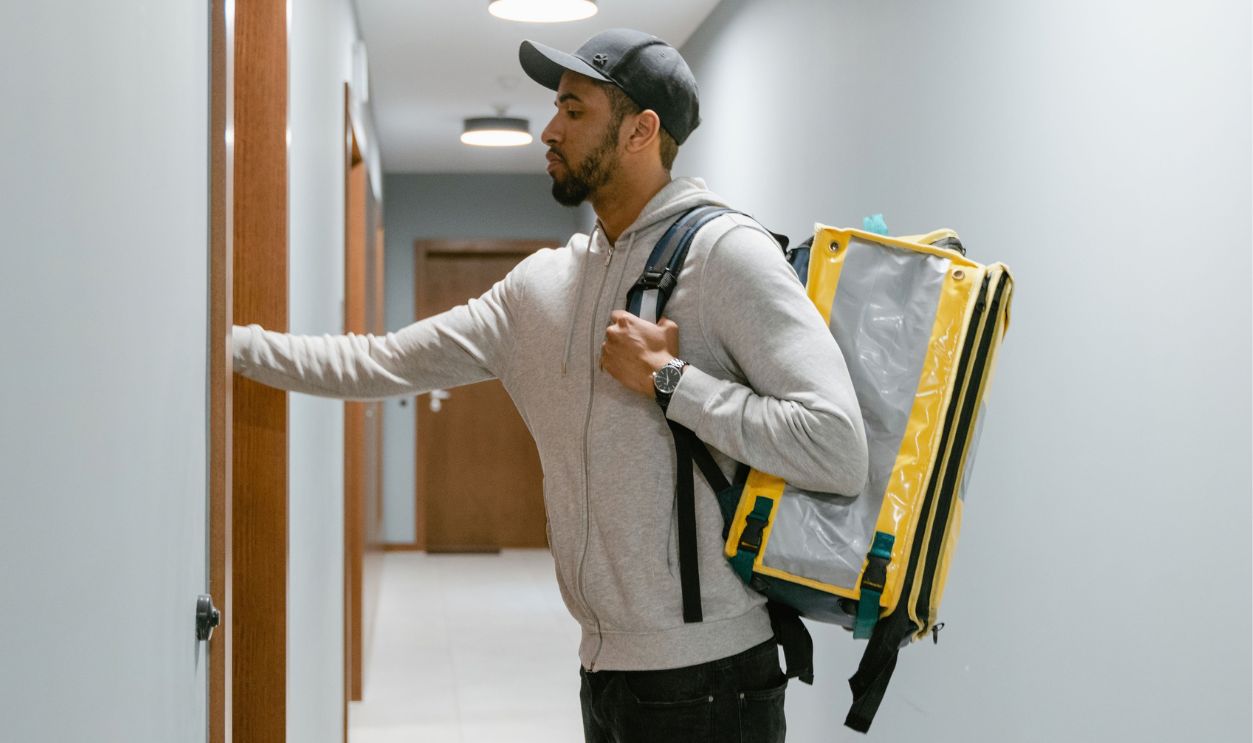 Courier wearing a backpack delivering food to an apartment door