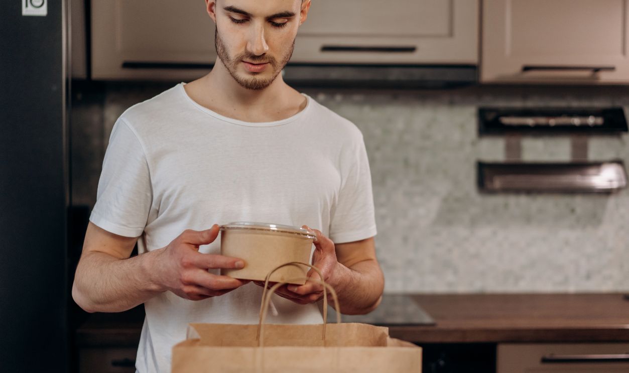 Adult man in a kitchen unpacking food delivery from a paper bag